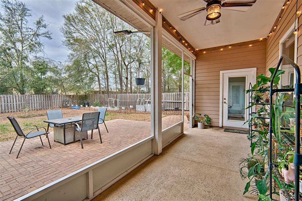 A screened-in patio features a brick floor, a ceiling fan, and a view of the backyard — 15122 NW 149TH ROAD, ALACHUA, FL