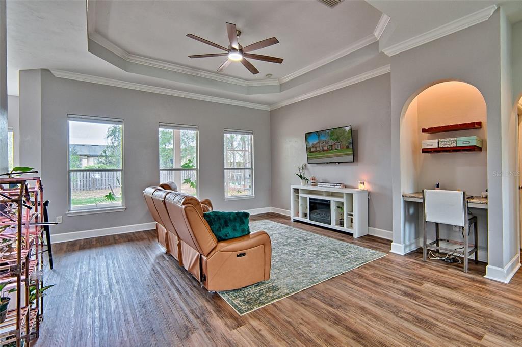 A living room features wood-look flooring, a tray ceiling, a television, and a built-in desk — 15122 NW 149TH ROAD, ALACHUA, FL