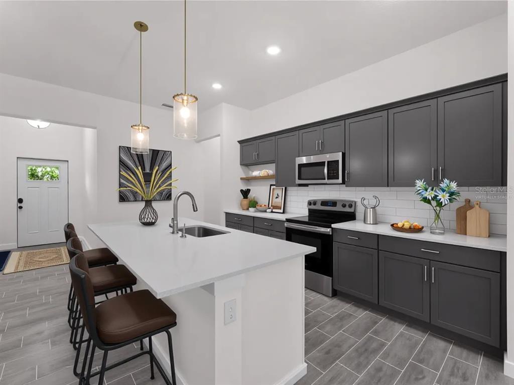 A modern kitchen features dark gray cabinets, a white island with seating, and tile flooring — 17339 ELMWOOD AVENUE, PORT CHARLOTTE, FL