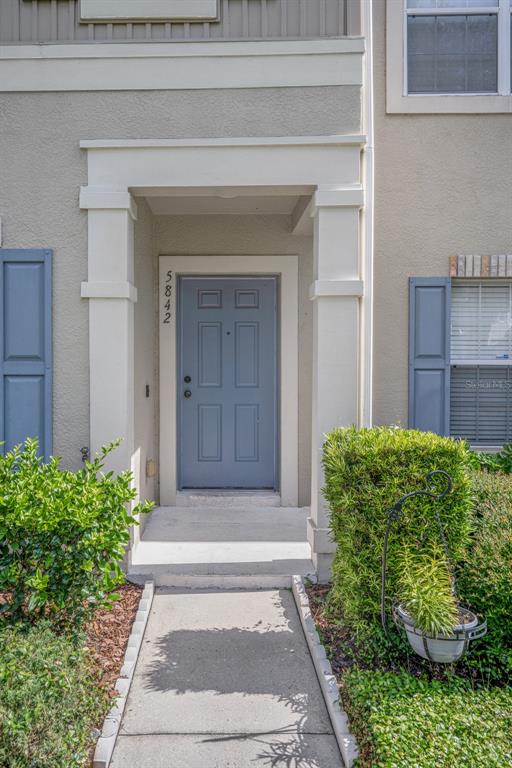 A gray front door is recessed under a white portico with a concrete walkway — 5842 FISHHAWK RIDGE DRIVE, LITHIA, FL