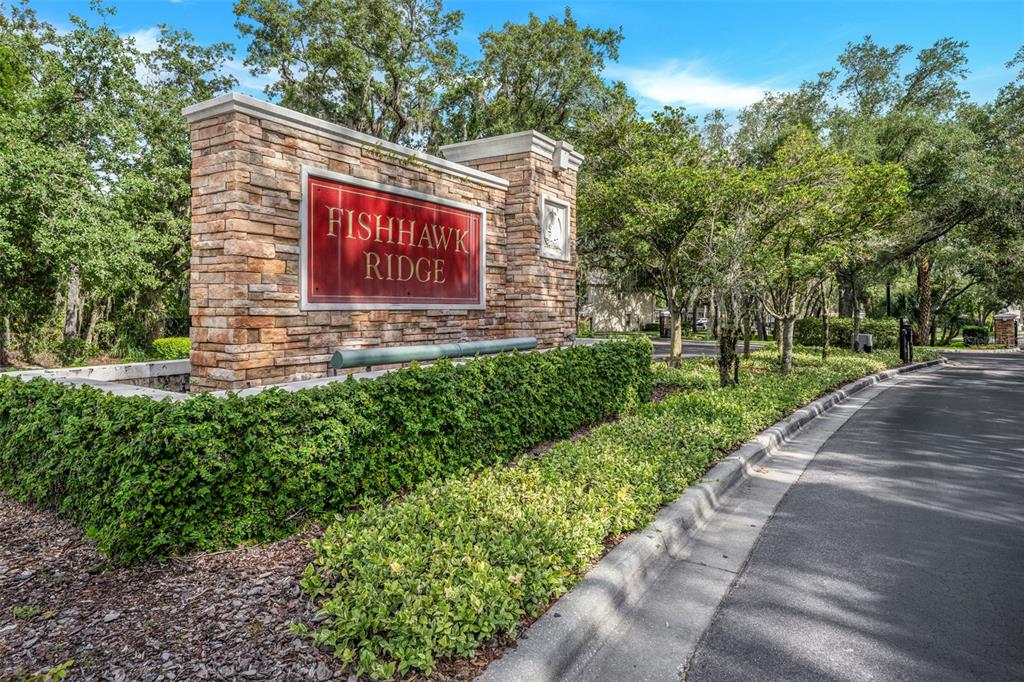 A stone monument sign for Fishhawk Ridge stands beside a paved road and landscaping — 5842 FISHHAWK RIDGE DRIVE, LITHIA, FL
