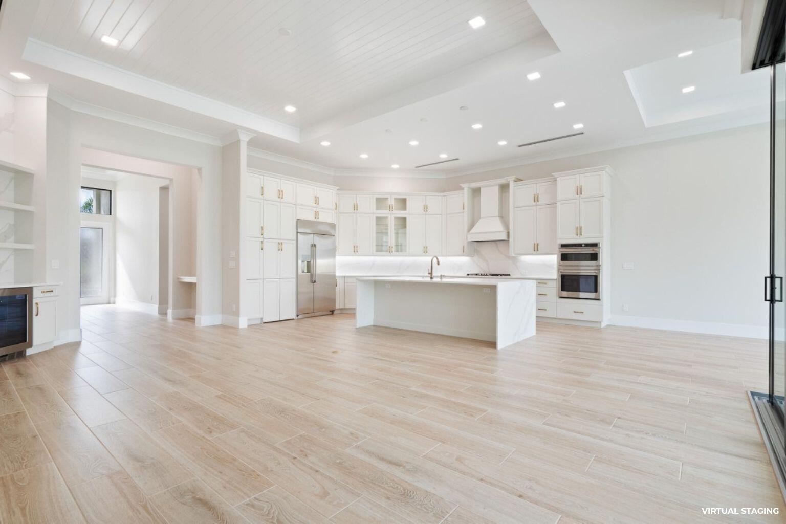 A spacious, modern white kitchen features a large marble island and light wood-look tile flooring — 7625 N Polo Grounds Lane, Vero Beach FL 32966, VERO BEACH, FL