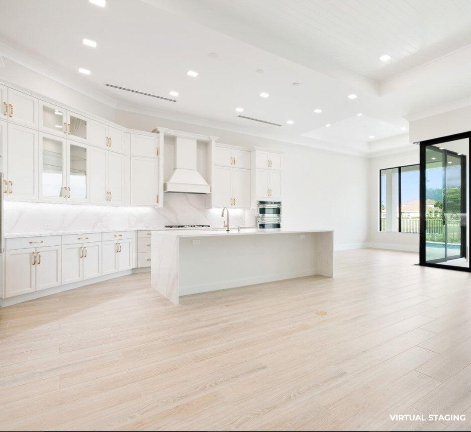 A bright, modern kitchen features white cabinetry, a large marble-topped island, and light wood flooring — 7625 N Polo Grounds Lane, Vero Beach FL 32966, VERO BEACH, FL