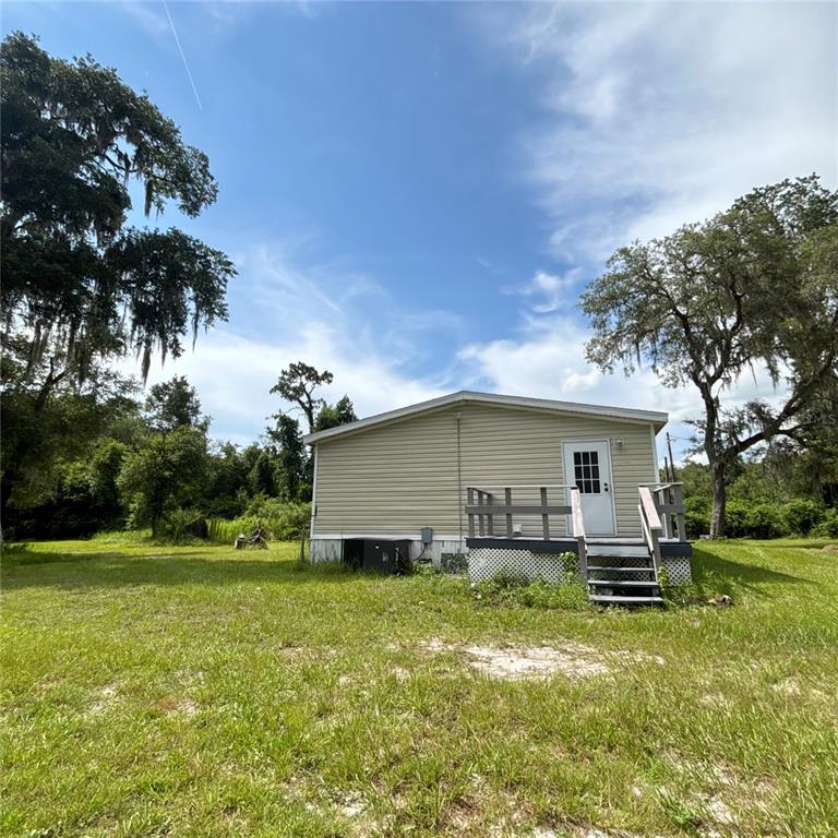 A single-story house with beige siding and a small wooden deck stands in a grassy yard — 12564 CR-681, WEBSTER, FL
