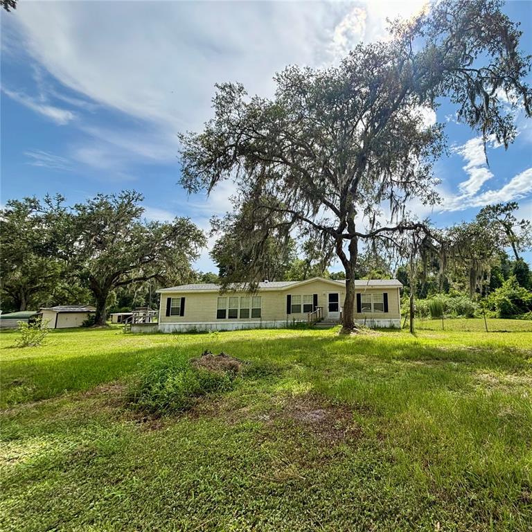 A single-story manufactured home sits on a grassy lot beneath large, moss-draped oak trees — 12564 CR-681, WEBSTER, FL