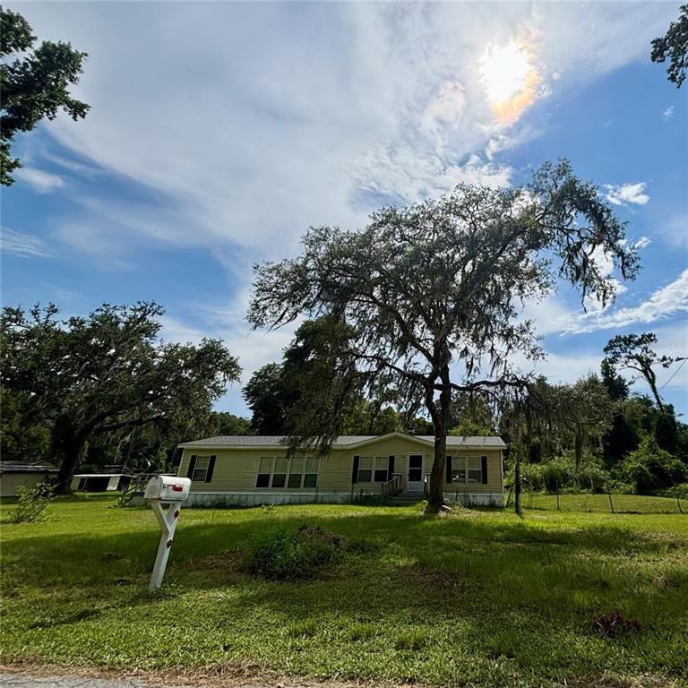 A single-story manufactured home sits on a grassy lot beneath large, moss-covered oak trees — 12564 CR-681, WEBSTER, FL