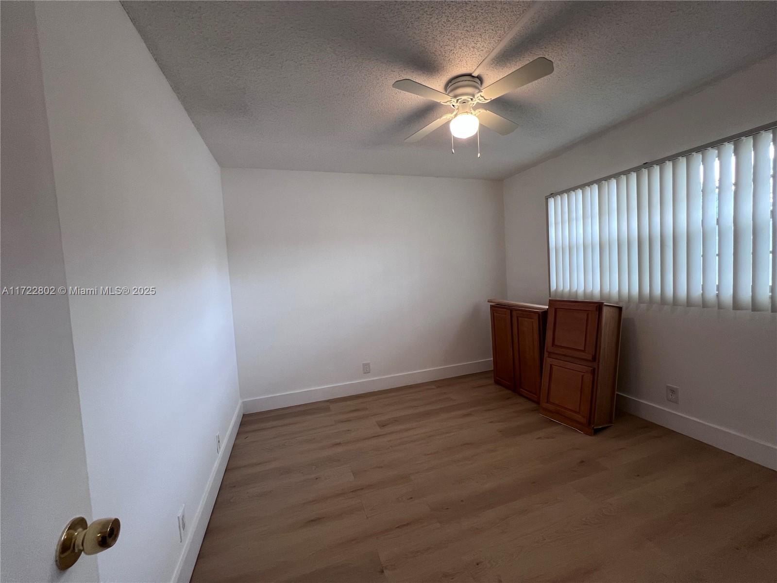 An empty room features white walls, wood-look flooring, a ceiling fan, and two wooden cabinets — 7400 NW 4th Pl # 106, Margate FL 33063, MARGATE, FL