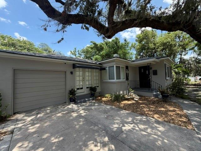 A single-story house with a garage, concrete driveway, and large overhanging tree branches — 1009 E MARKS STREET, ORLANDO, FL