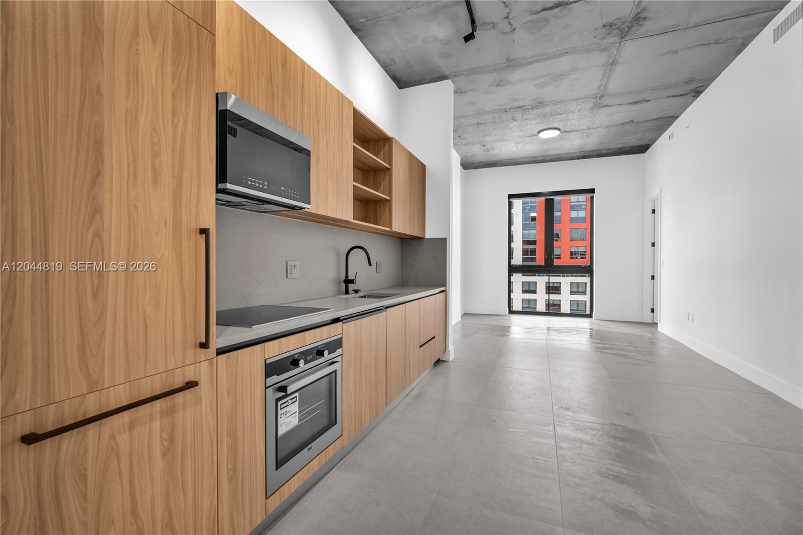 A modern kitchen features light wood cabinetry, stainless steel appliances, and a concrete ceiling — 91 NW 27th St # 204, Miami FL 33127, MIAMI, FL