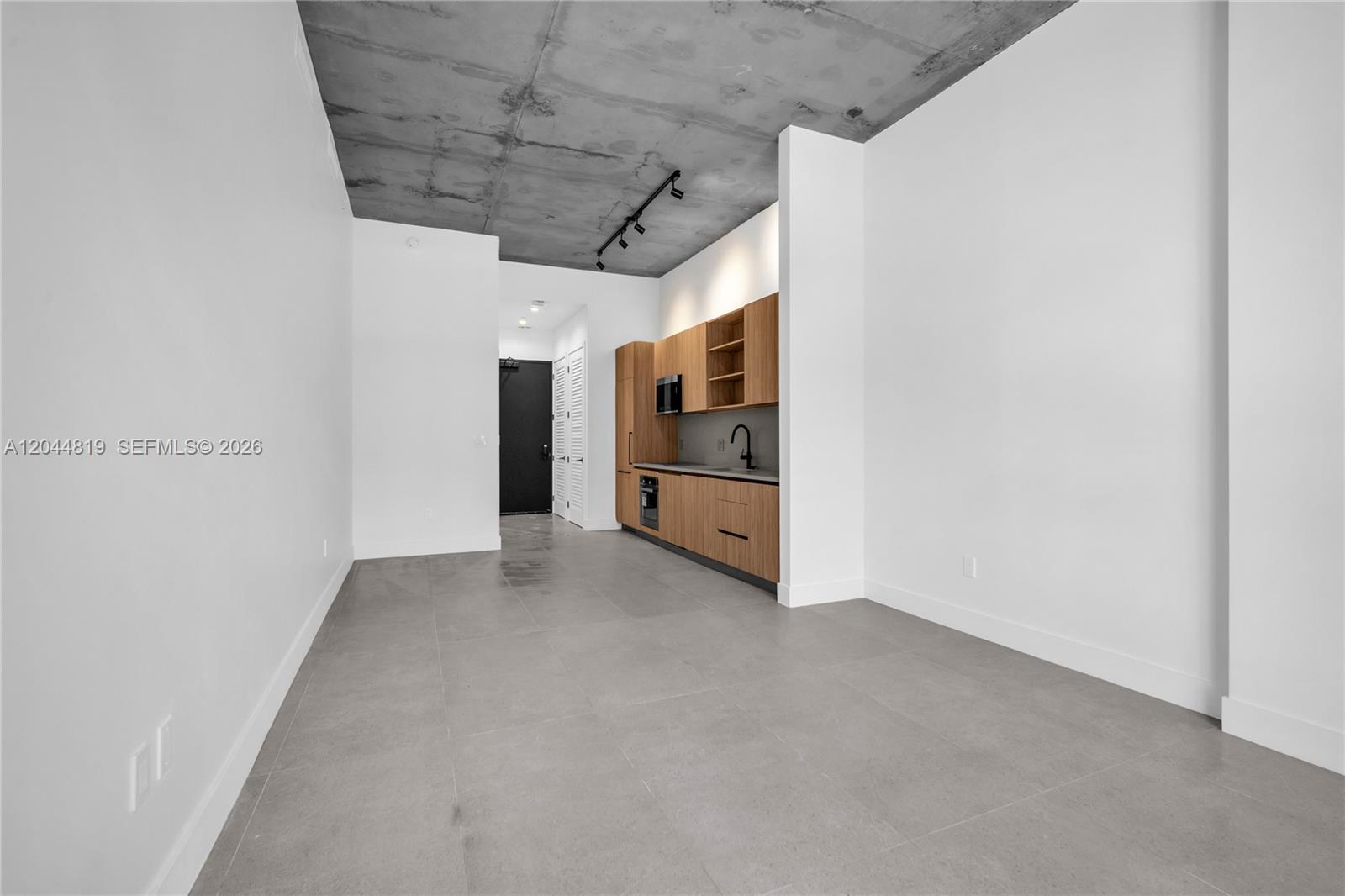 This modern studio apartment features a concrete ceiling, gray tile floors, and a kitchenette — 91 NW 27th St # 204, Miami FL 33127, MIAMI, FL