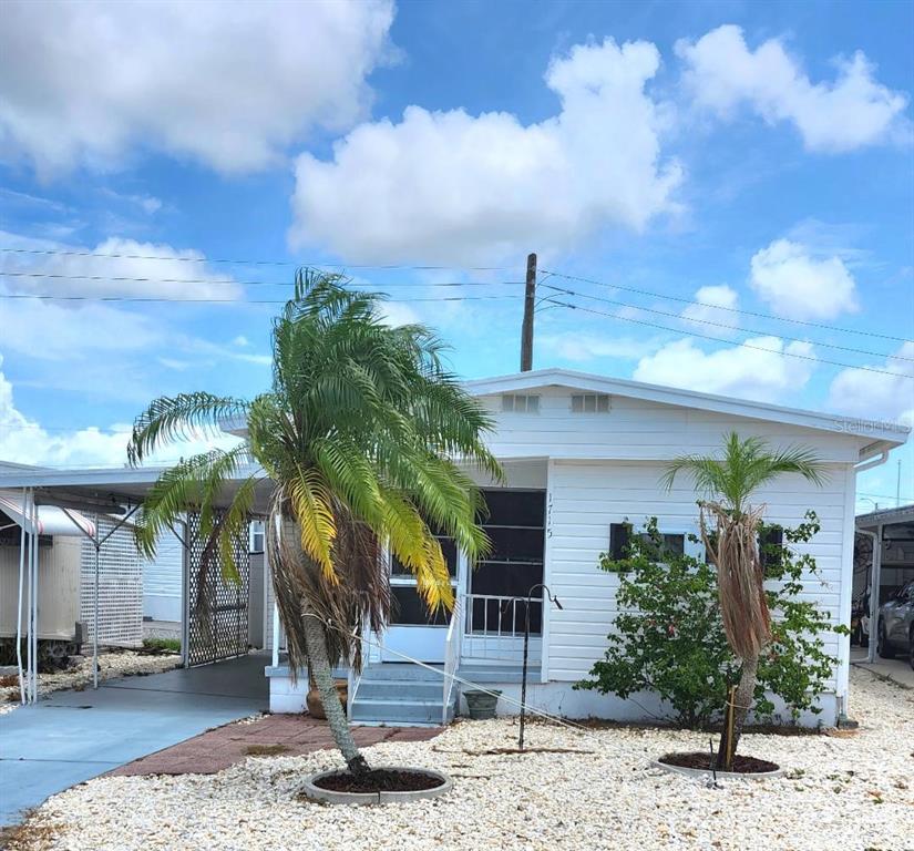 A white mobile home features a covered carport, a small front porch, and two palm trees — 1715 ILLINOIS AVENUE, BRADENTON, FL