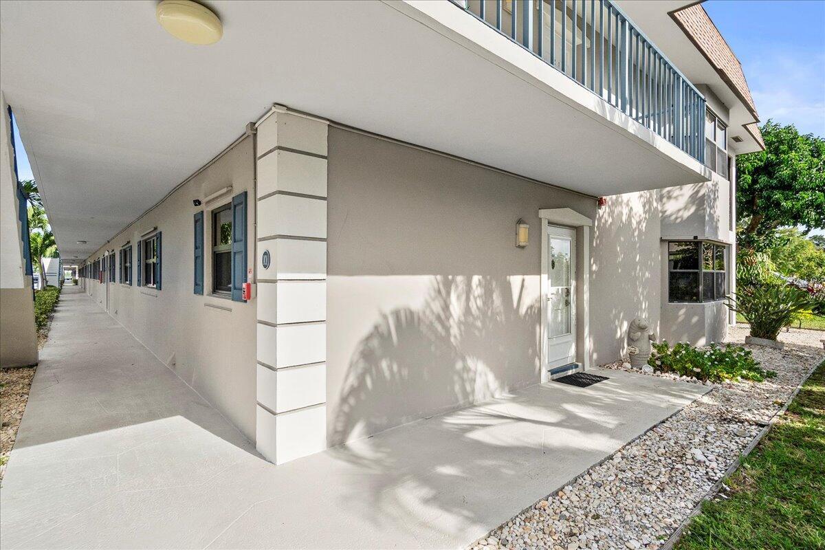 An exterior view of a ground-level apartment entrance with a concrete walkway and balcony above — 755 Saturn Street # H101, Jupiter FL 33477, JUPITER, FL