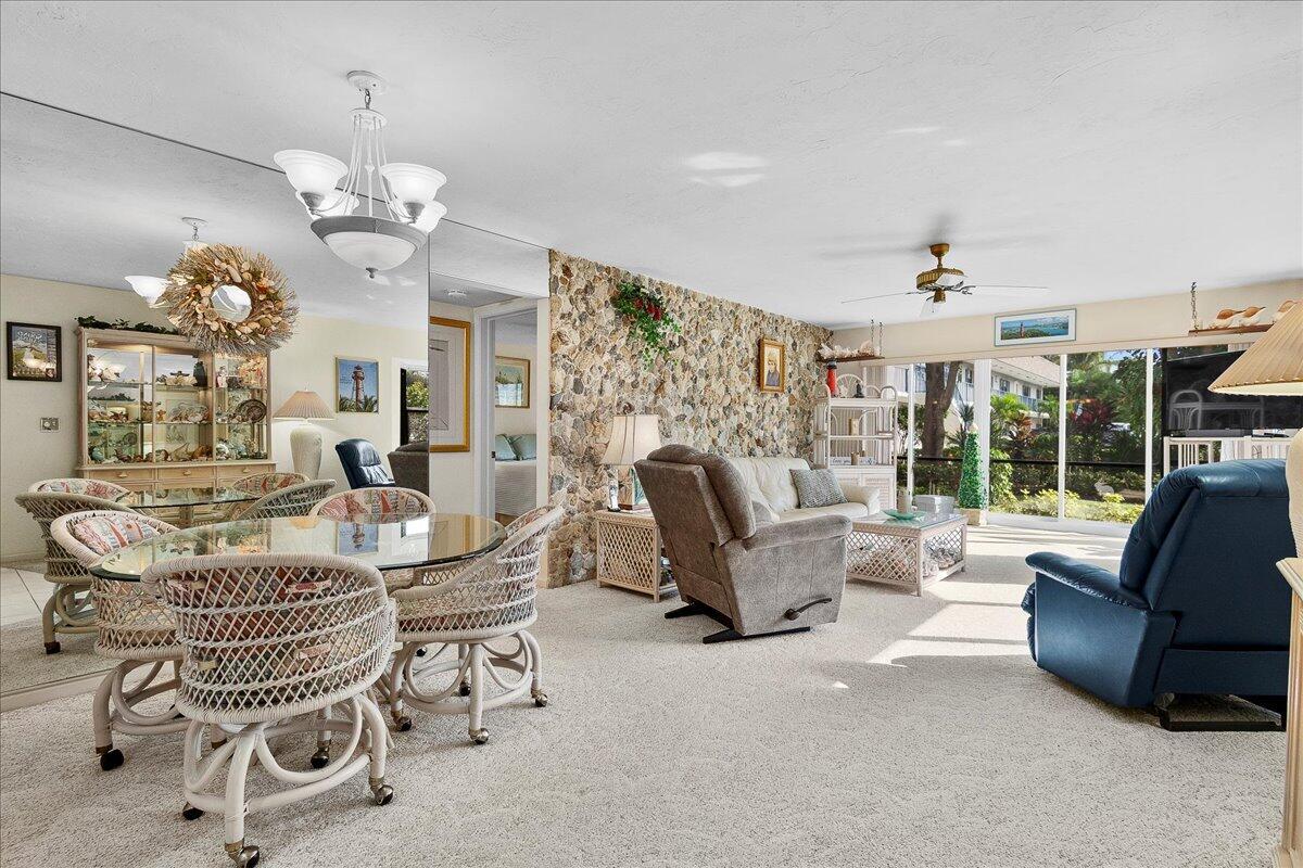 A living and dining area features a stone accent wall, carpeted floors, and large windows — 755 Saturn Street # H101, Jupiter FL 33477, JUPITER, FL