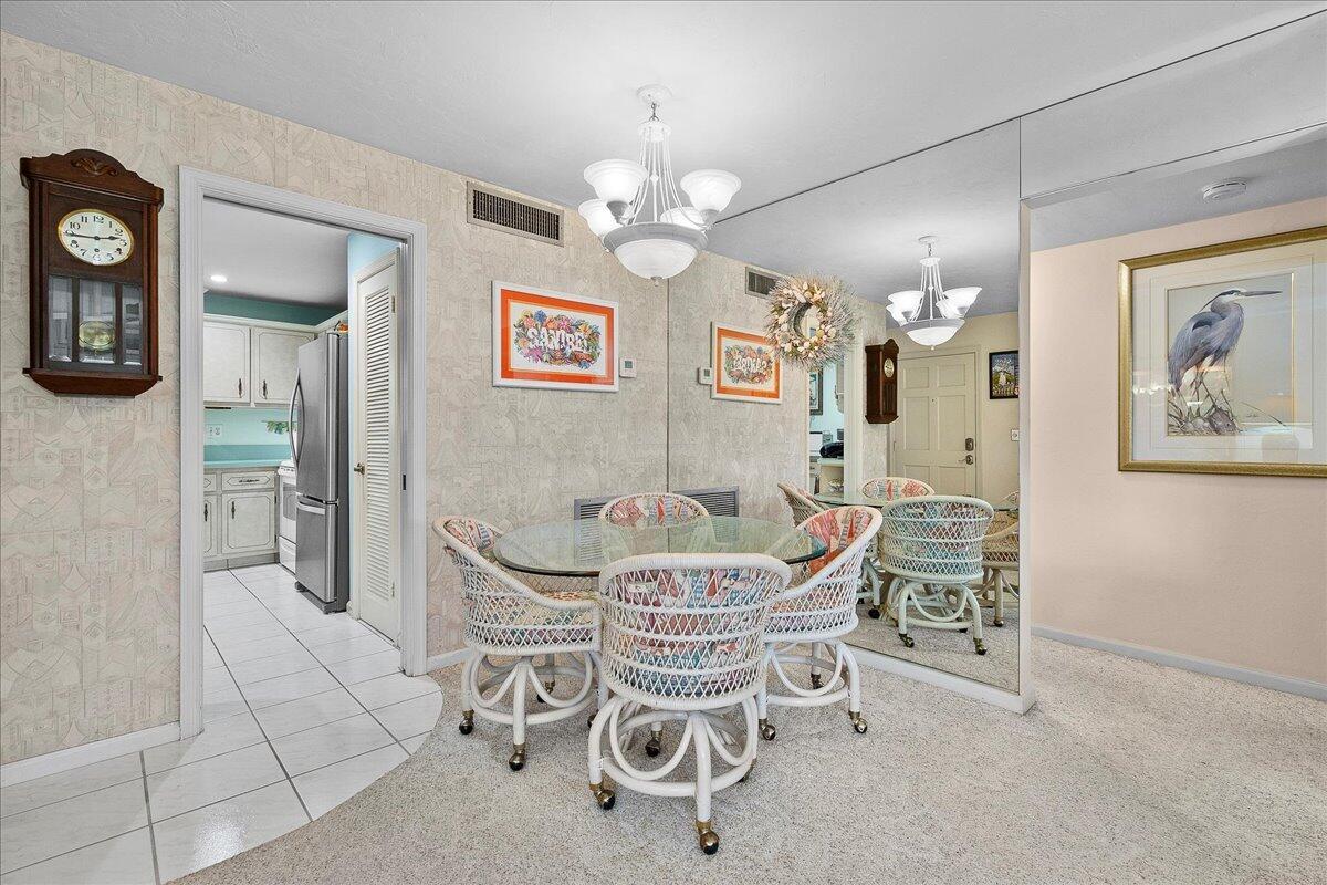 A dining area features a glass-topped wicker table, patterned wallpaper, and a large wall mirror — 755 Saturn Street # H101, Jupiter FL 33477, JUPITER, FL