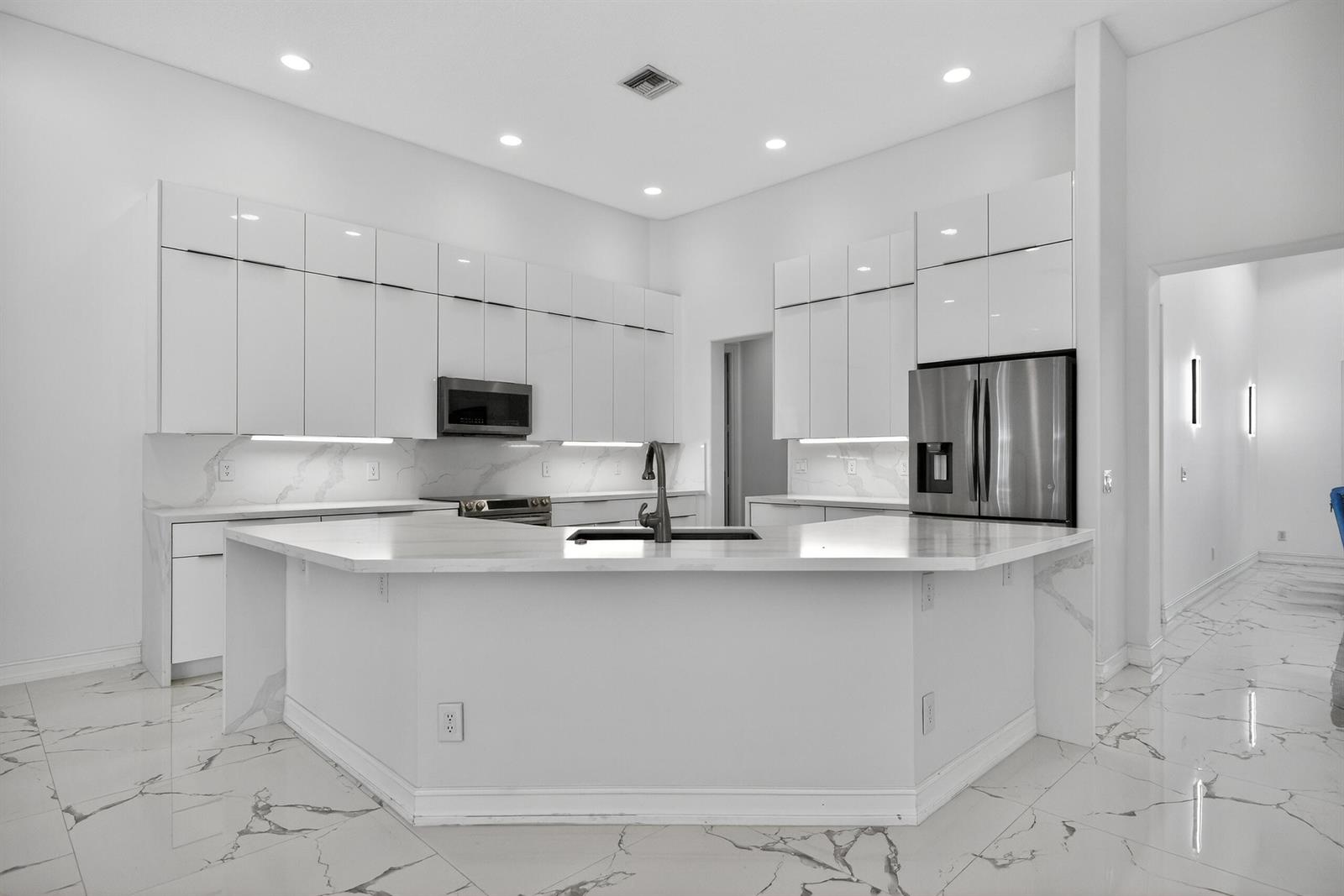 A modern white kitchen features marble countertops, high-gloss cabinetry, and a large central island — 14780 Horseshoe Trace, Wellington FL 33414, WELLINGTON, FL