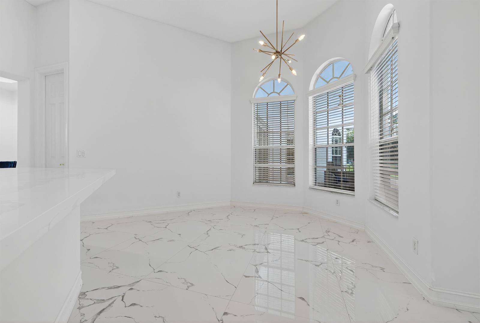 A bright dining area features white marble-look tile flooring, arched windows, and a modern chandelier — 14780 Horseshoe Trace, Wellington FL 33414, WELLINGTON, FL