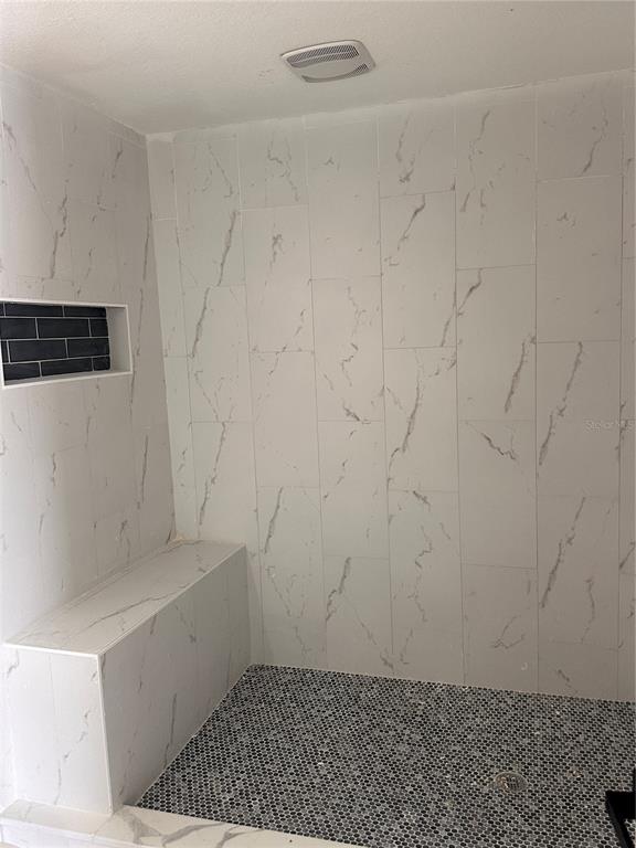 A walk-in shower features white marble-look wall tiles, a built-in bench, and dark mosaic flooring — 1716 SPRUCEWOOD LANE, ORLANDO, FL
