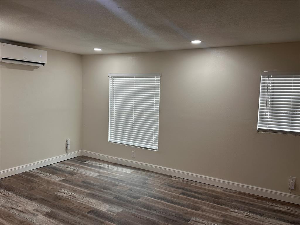A room with wood-look flooring, two windows with white blinds, and a wall-mounted air conditioner — 1716 SPRUCEWOOD LANE, ORLANDO, FL