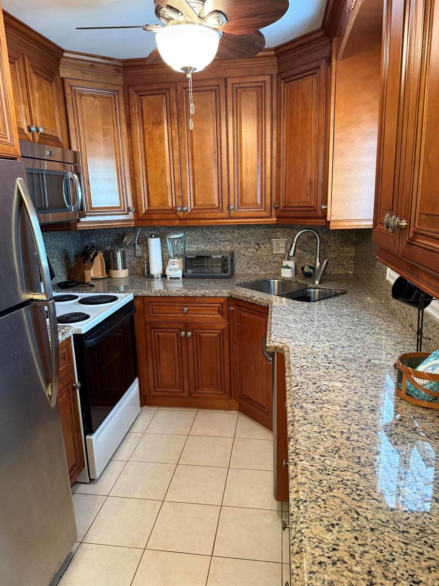 A kitchen features wood cabinets, granite countertops, stainless steel appliances, and tile flooring — 3160 Lake Osborne Drive # 112, FL 33461, FL