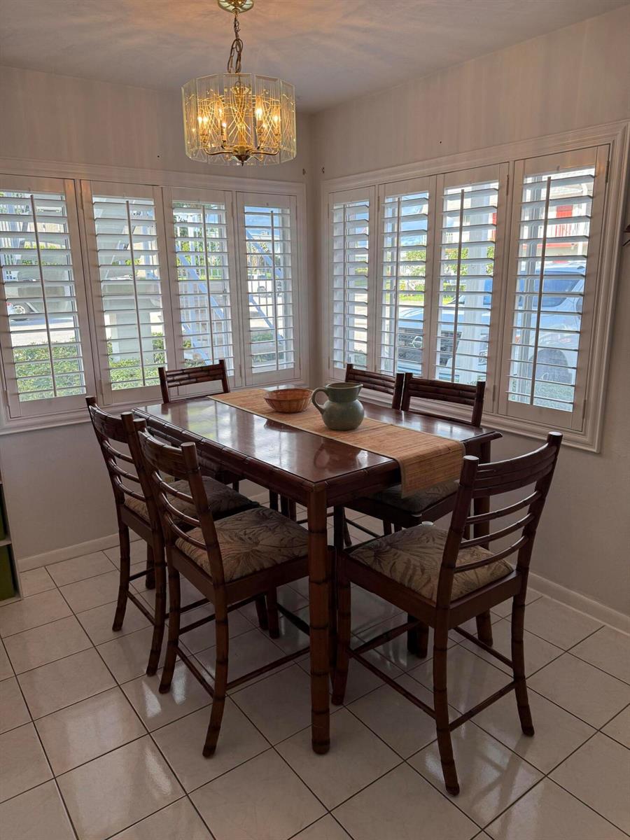 A dining room with a wooden table, bamboo-style chairs, tile flooring, and white plantation shutters — 3160 Lake Osborne Drive # 112, FL 33461, FL
