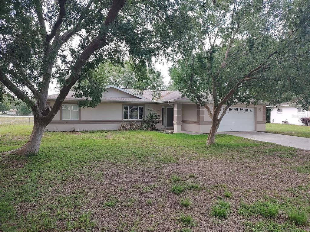 A single-story house with a white garage and two large trees in the front yard — 6202 SW 100TH LOOP, OCALA, FL