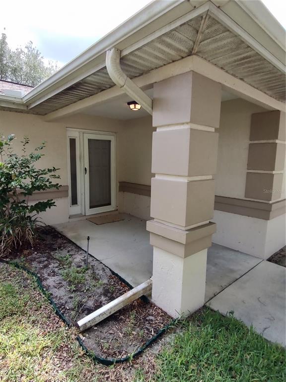 A covered front porch features a white door, a light fixture, and a concrete floor — 6202 SW 100TH LOOP, OCALA, FL