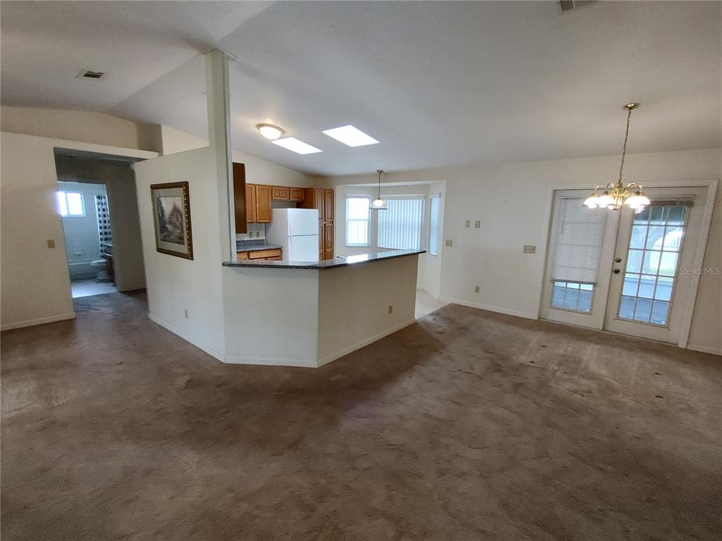 An open-concept living area features a kitchen with wood cabinets, a breakfast bar, and carpet — 6202 SW 100TH LOOP, OCALA, FL