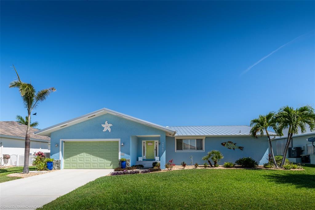 A light blue single-story house with a green garage door and palm trees in front — 2060 VIA SEVILLE, PUNTA GORDA, FL