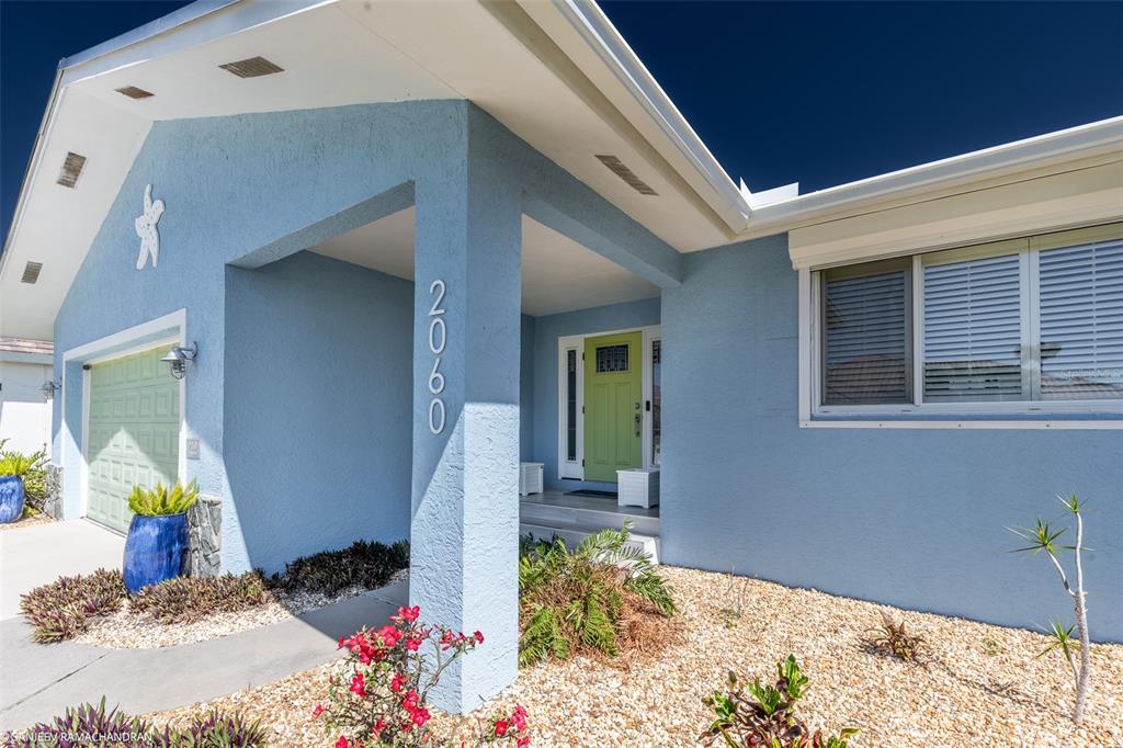 A light blue house exterior features a green front door and a column displaying house numbers — 2060 VIA SEVILLE, PUNTA GORDA, FL