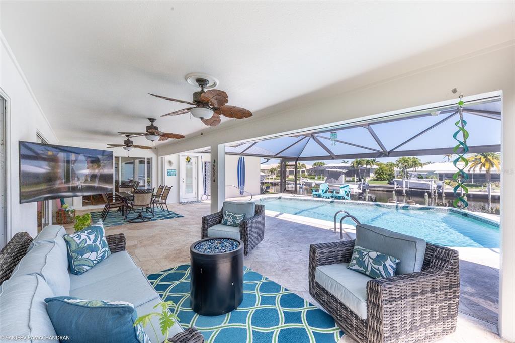 A covered patio features wicker furniture, a fire pit, and a pool overlooking a canal — 2060 VIA SEVILLE, PUNTA GORDA, FL