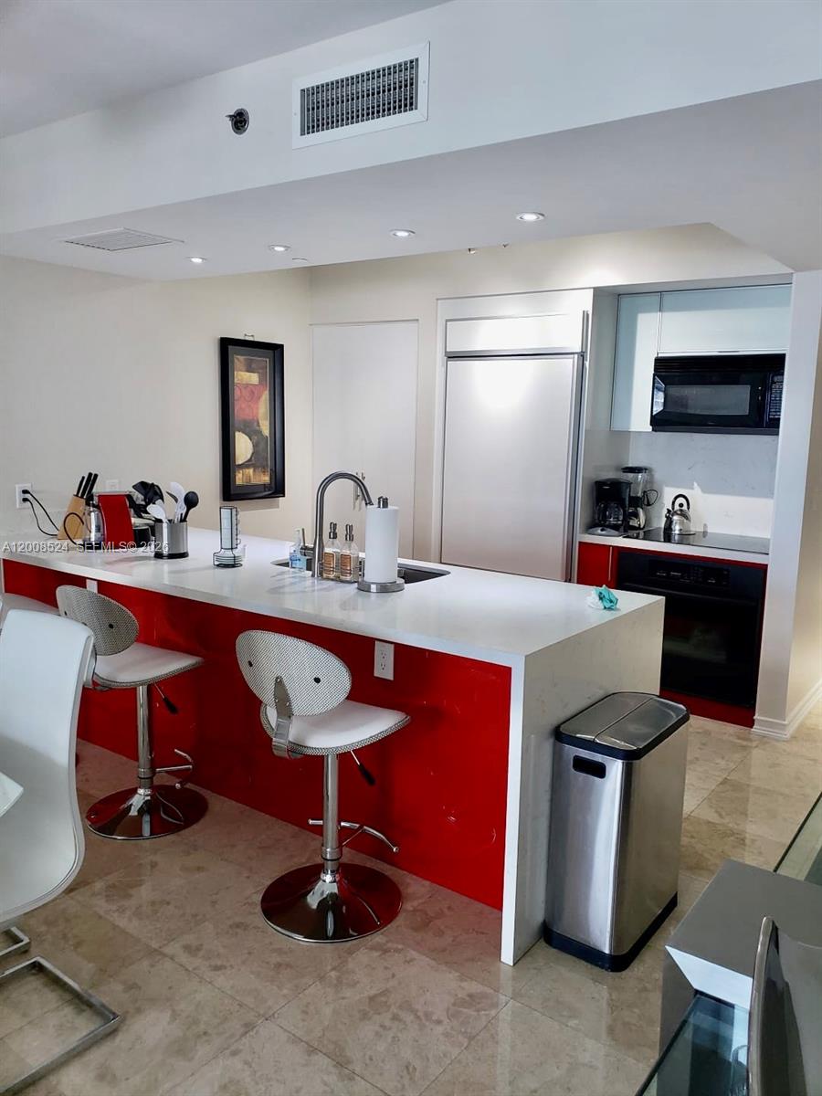 A kitchen features a red island with white countertops, bar stools, and stainless steel appliances — 1830 S OCEAN DR # 3910, Hallandale Beach FL 33009, HALLANDALE BEACH, FL