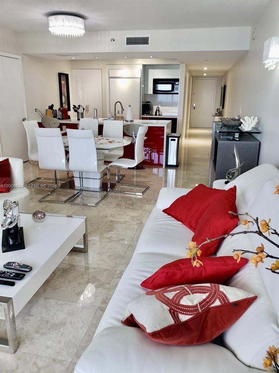 A modern open-concept living and dining area features white furniture, red accents, and marble flooring — 1830 S OCEAN DR # 3910, Hallandale Beach FL 33009, HALLANDALE BEACH, FL