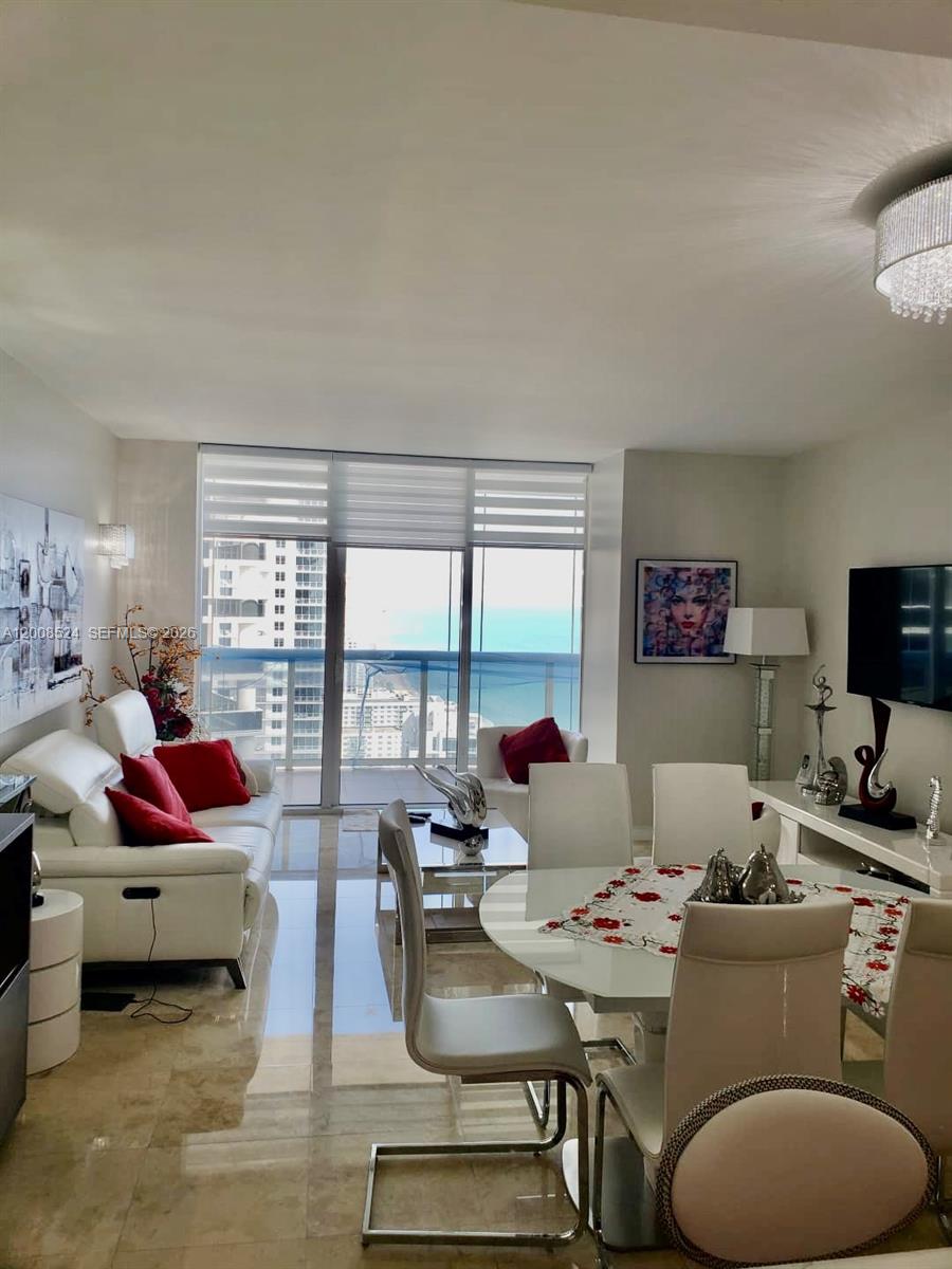 A living and dining area features white furniture, red accents, and a balcony overlooking the ocean — 1830 S OCEAN DR # 3910, Hallandale Beach FL 33009, HALLANDALE BEACH, FL