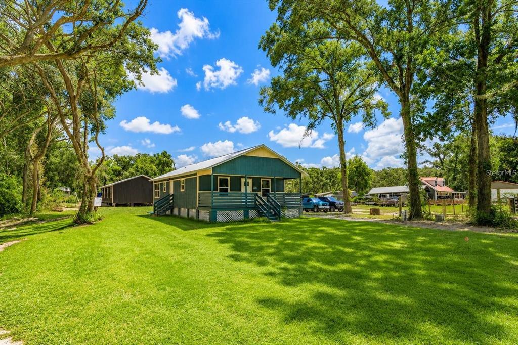 A teal-sided house with a front porch sits on a grassy lot among many trees — 4839 CR 686, WEBSTER, FL
