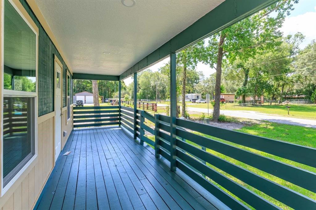 A covered wooden porch with dark green railings overlooks a grassy yard and trees — 4839 CR 686, WEBSTER, FL