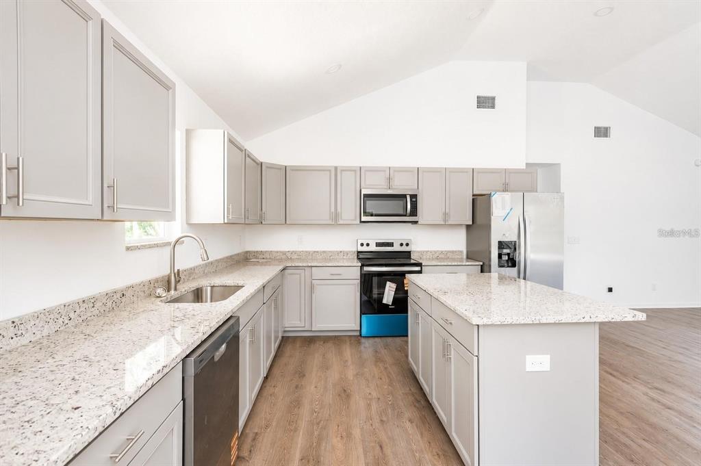 A kitchen features light gray cabinets, granite countertops, stainless steel appliances, and wood-look flooring — 4839 CR 686, WEBSTER, FL