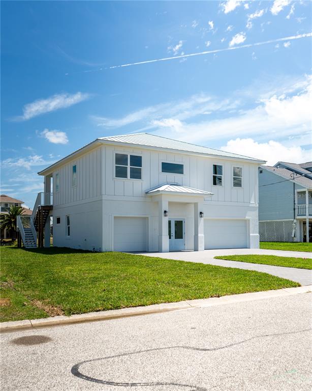A two-story white house with a metal roof and two garage doors sits on grass — 4050 JEWFISH DRIVE, HUDSON, FL