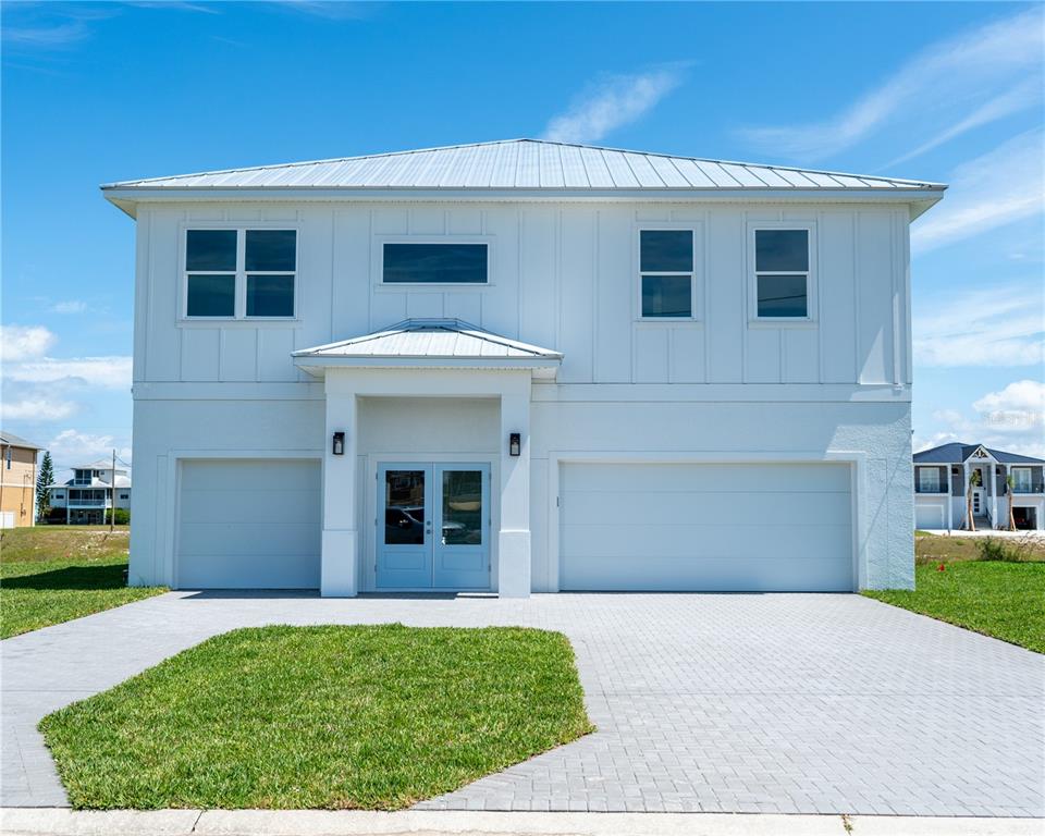 A two-story white house with a metal roof, two garage doors, and a paved driveway — 4050 JEWFISH DRIVE, HUDSON, FL