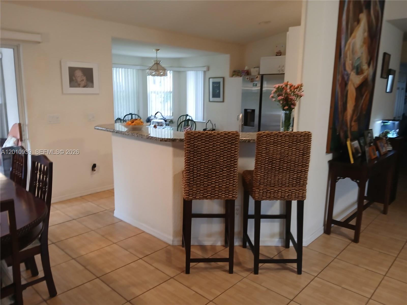 A kitchen features a granite breakfast bar with two woven barstools and tile flooring — 5880 SW 102, Ocala FL 34476, OCALA, FL