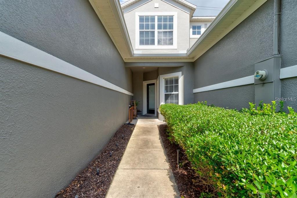 A concrete walkway leads to a front entrance flanked by gray walls and green hedges — 1128 TRAVERTINE TERRACE, SANFORD, FL