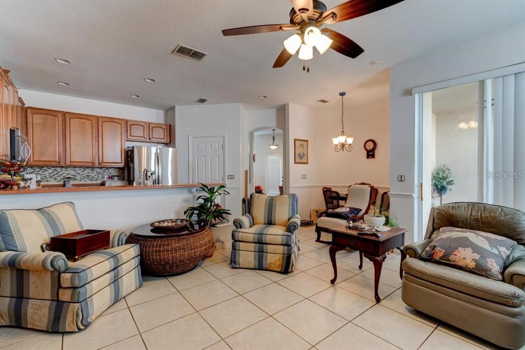 A living room with tile floors, a ceiling fan, and a kitchen counter in view — 1128 TRAVERTINE TERRACE, SANFORD, FL