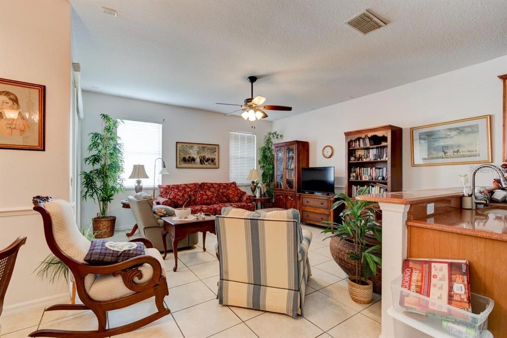 A living room features tile flooring, a ceiling fan, a red sofa, and a bookshelf — 1128 TRAVERTINE TERRACE, SANFORD, FL