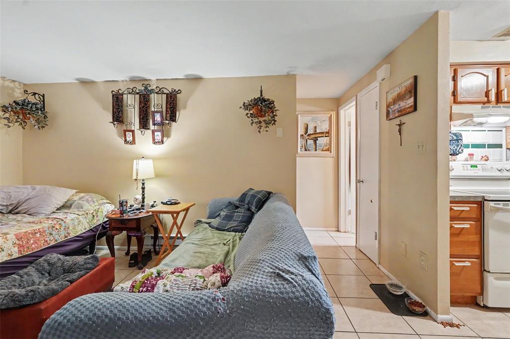 A living room with a bed, a blue sofa, and a tiled floor leads to a kitchen — 5513 OCEANIC ROAD, HOLIDAY, FL