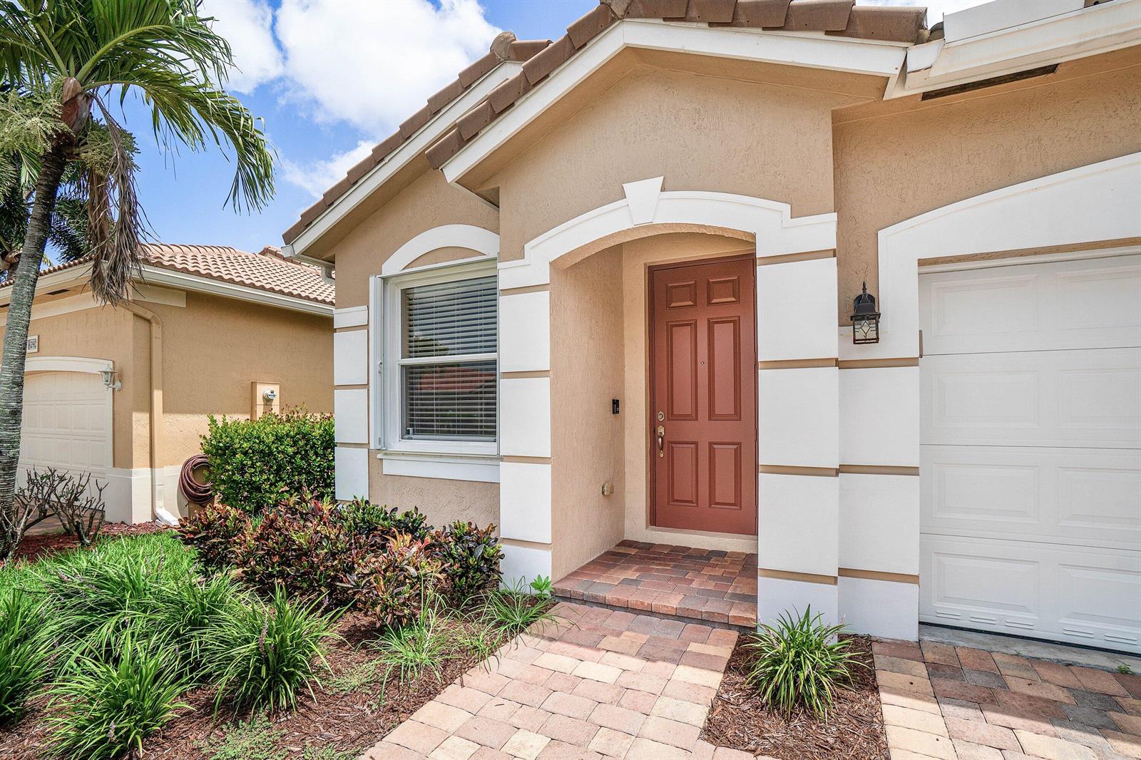 The exterior of a tan house features a brown front door, white trim, and pavers — 4250 Key Lime Boulevard, Boynton Beach FL 33436, BOYNTON BEACH, FL