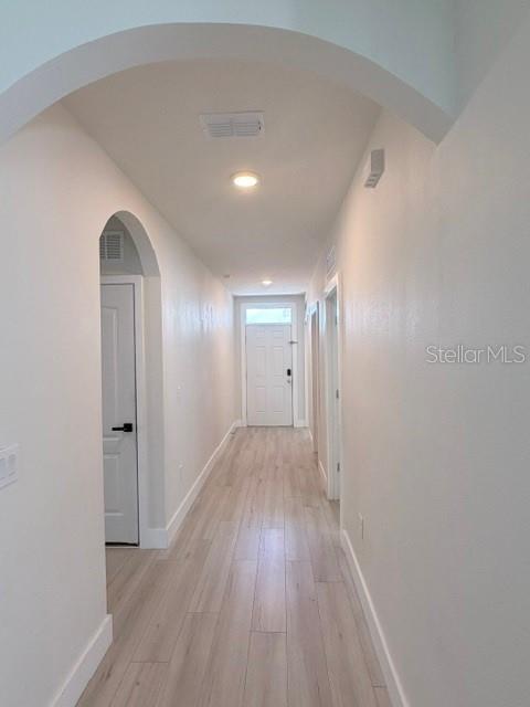 A hallway with light wood-look flooring leads to a white front door under an archway — 1776 RANGER HIGHLANDS ROAD, KISSIMMEE, FL