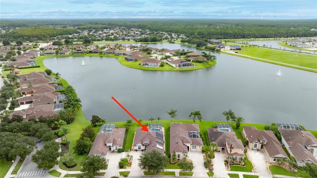 An aerial view shows a suburban house with a pool cage beside a large lake — 3385 TESORO CIRCLE, NEW SMYRNA BEACH, FL