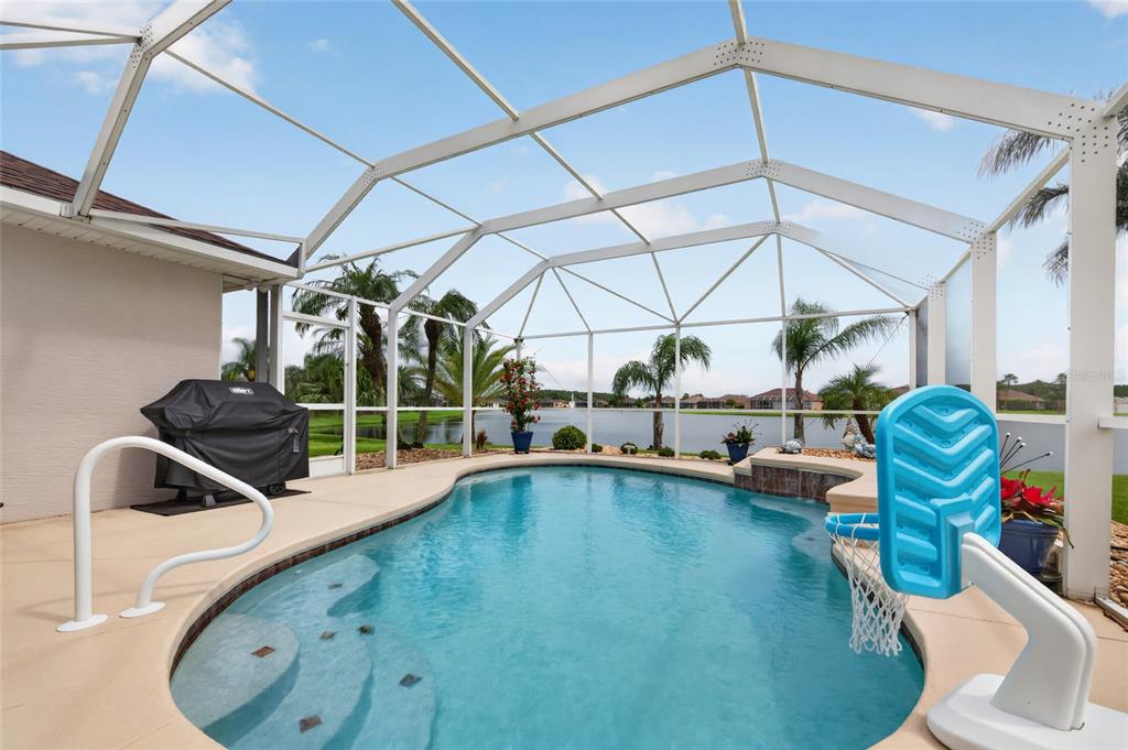A screened-in pool area with a basketball hoop, grill, and a view of a lake — 3385 TESORO CIRCLE, NEW SMYRNA BEACH, FL
