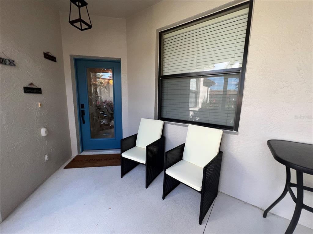 A covered porch features two black wicker chairs with white cushions and a blue door — 2522 OSWEGO DRIVE, NORTH PORT, FL