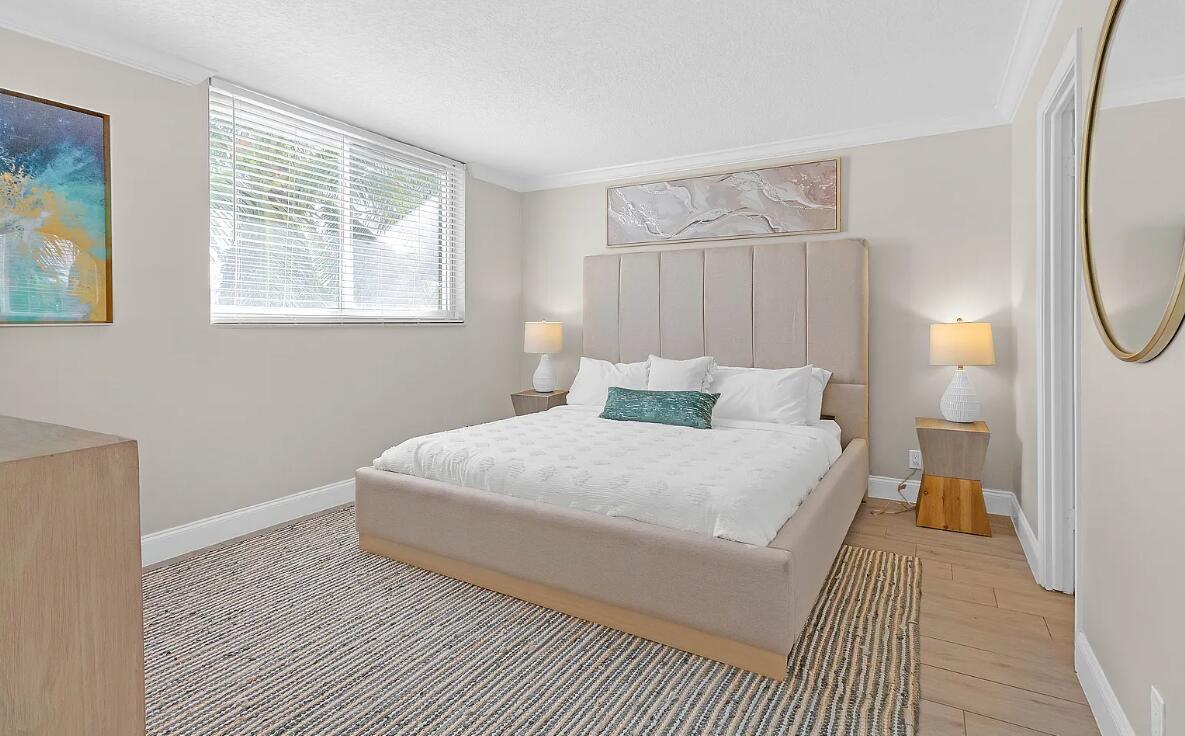 A bedroom features a beige upholstered bed, a jute rug, and two bedside lamps — 601 N Ocean Boulevard, Boca Raton FL 33432, BOCA RATON, FL