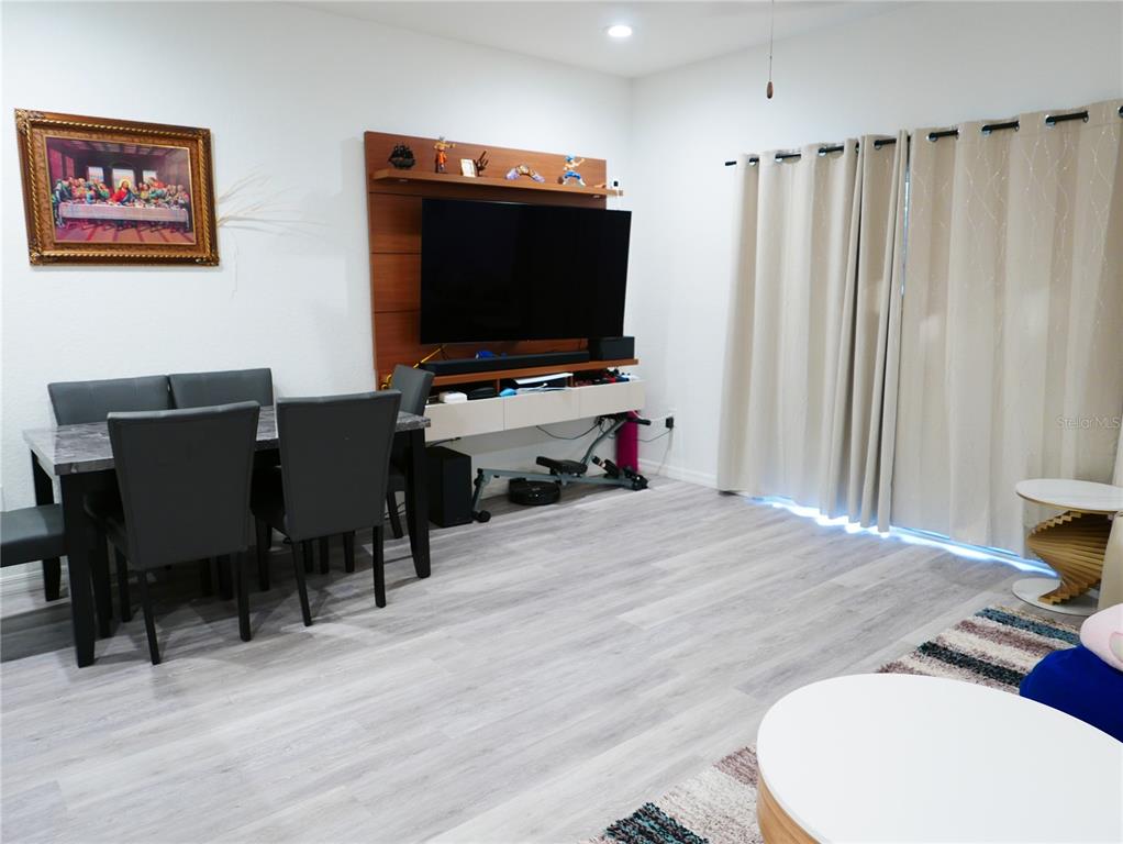 A dining area and living space feature light wood-look flooring, a wall-mounted television, and curtains — 4769 VIGNETTE WAY, SARASOTA, FL